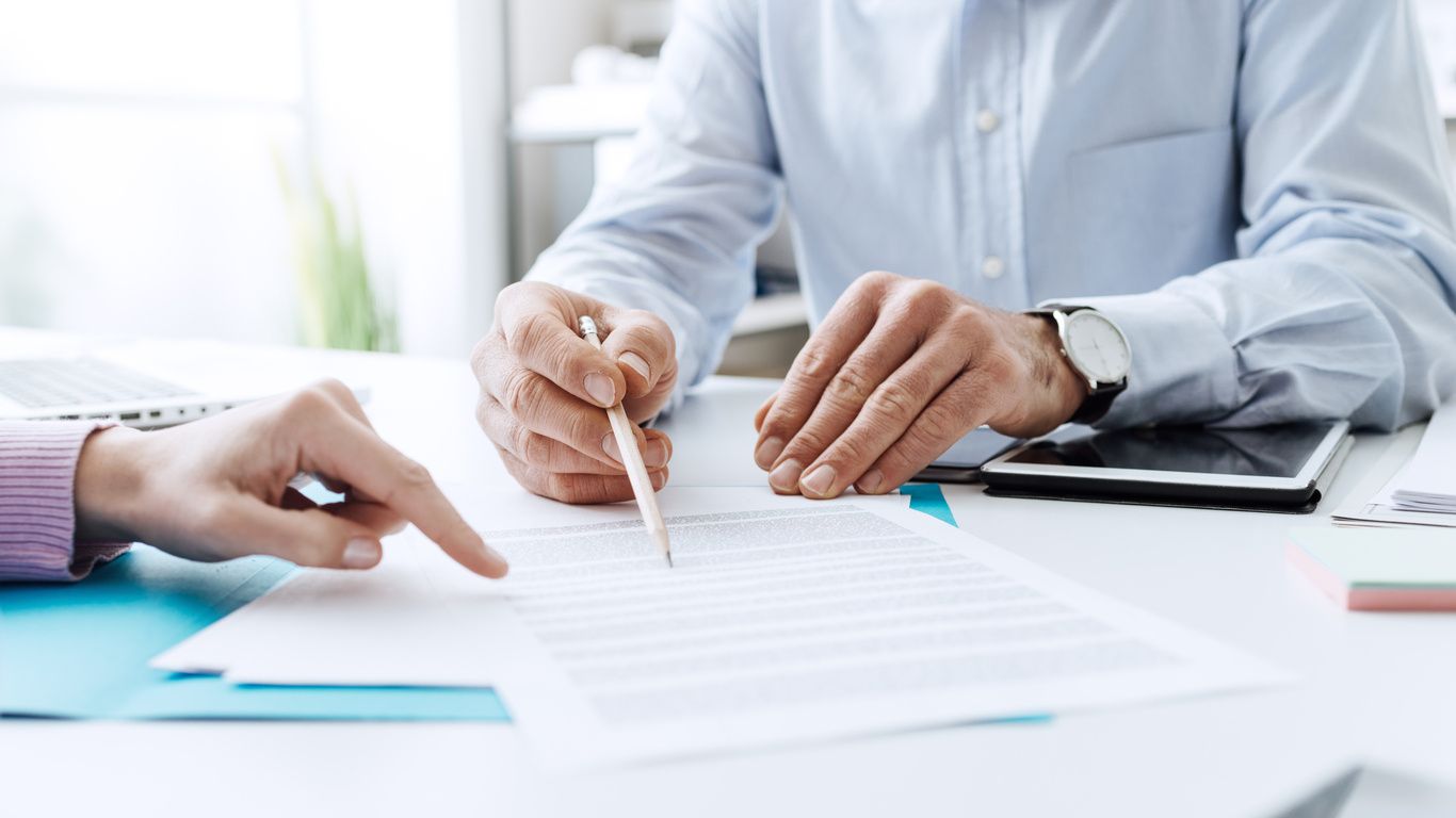 Two people are working on a paper with one hand and the other holding a pencil.
